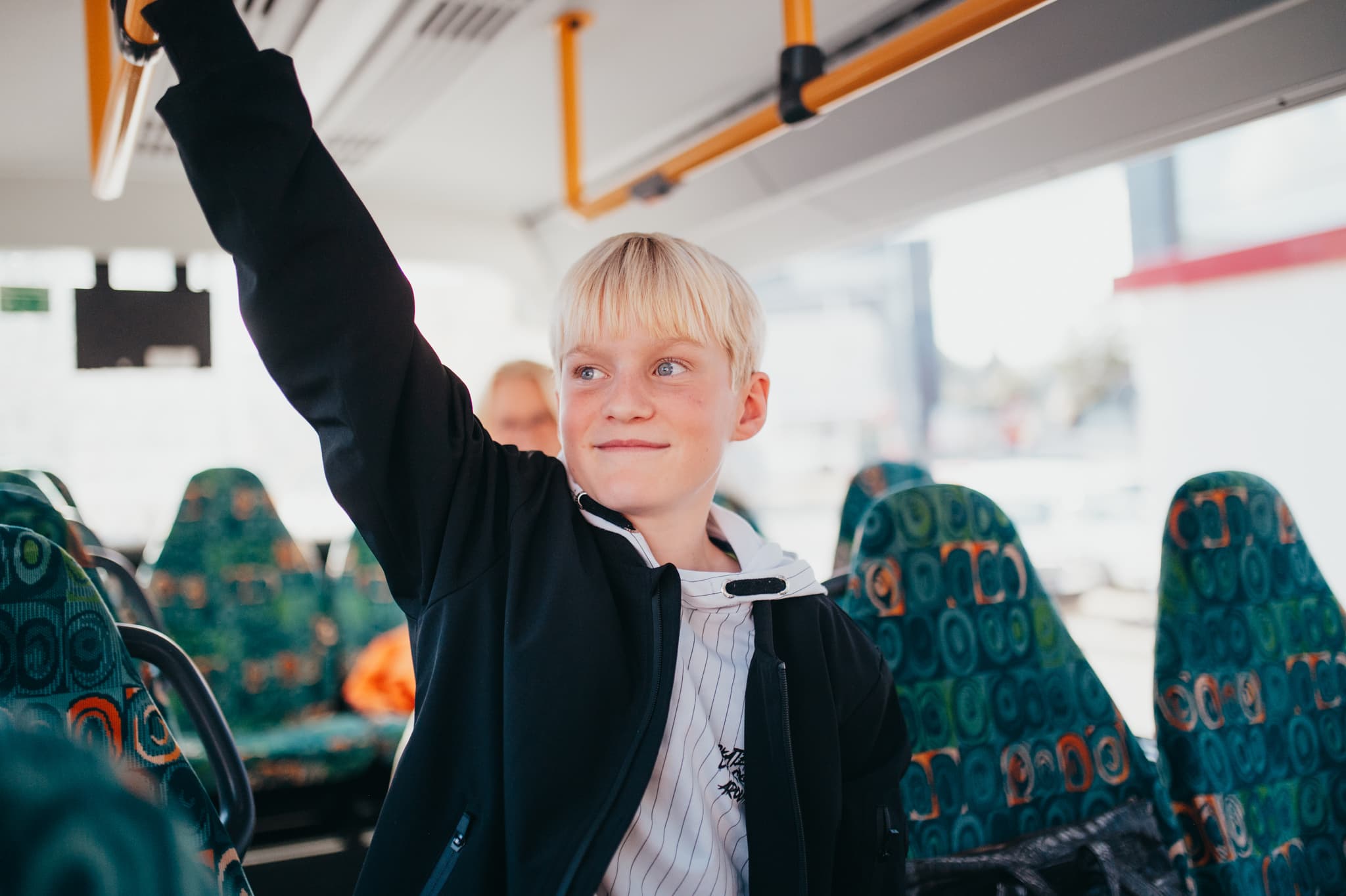 Kind hält sich während der Fahrt an einem Haltegriff im Bus fest